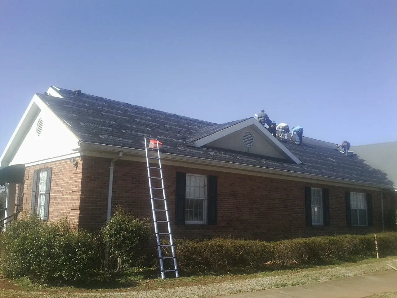 Crew tearing shingles off a brick ranch roof with a ladder set — Metal Roof Repair work by our crew in Alexander