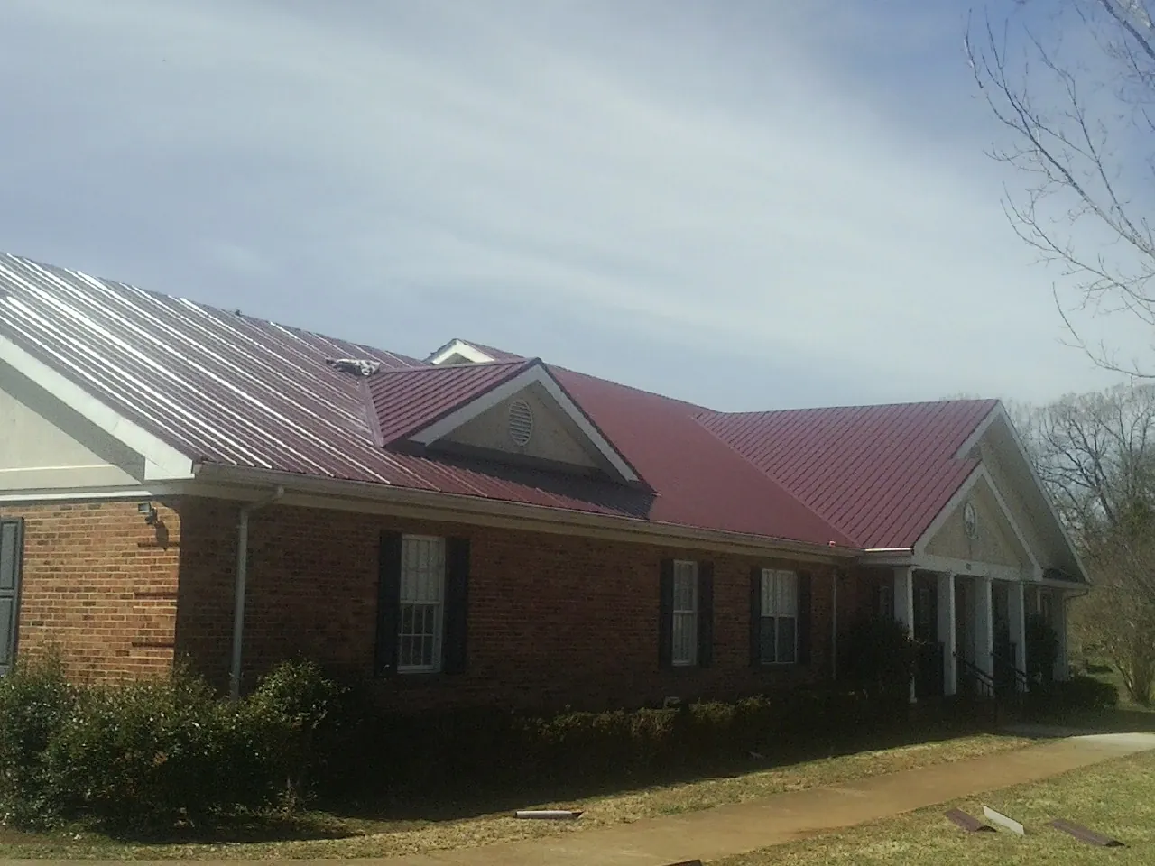 Red metal roof with gabled entries on a long brick building, from a Hail Damage Roof Repair job in Alexander