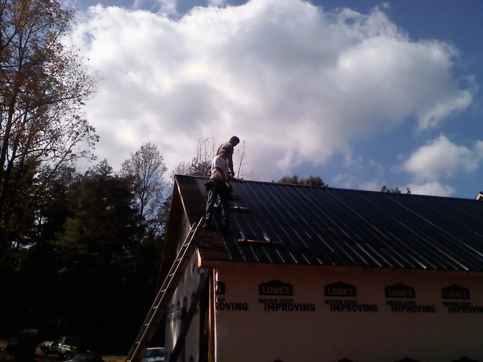 Roofer fastening dark metal panels high against a cloudy sky, from a Roof Inspection job in Alexander