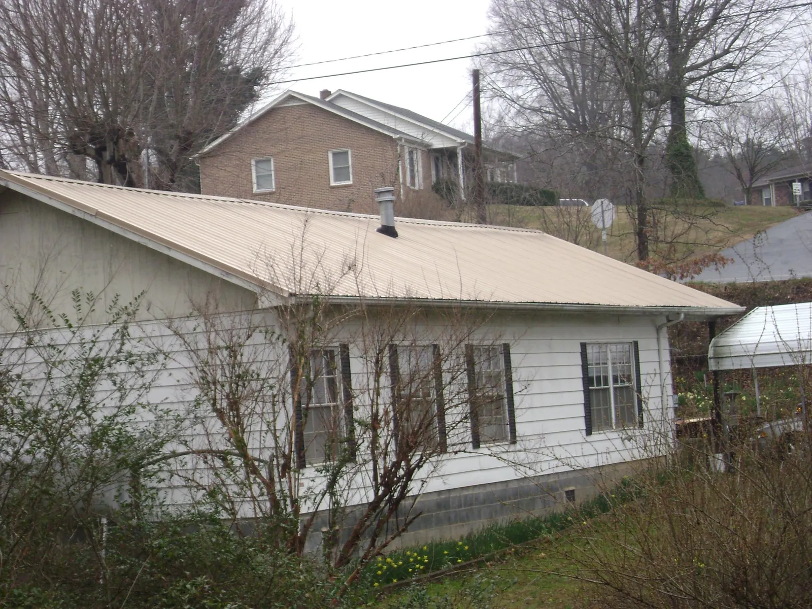 Tan metal roof on a white sided house set into a hillside — Commercial Roofing by Roofing Brothers in Alexander